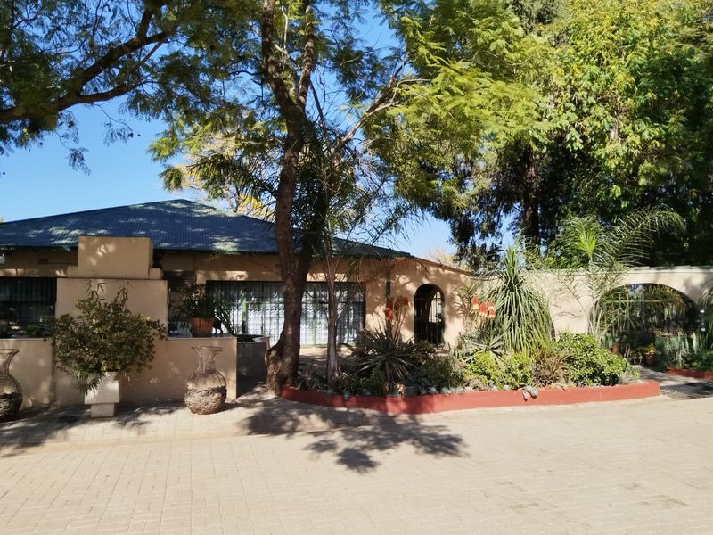 Front elevation of a farm-style residence featuring a paved driveway, mature trees, and an arched entrance with security features.