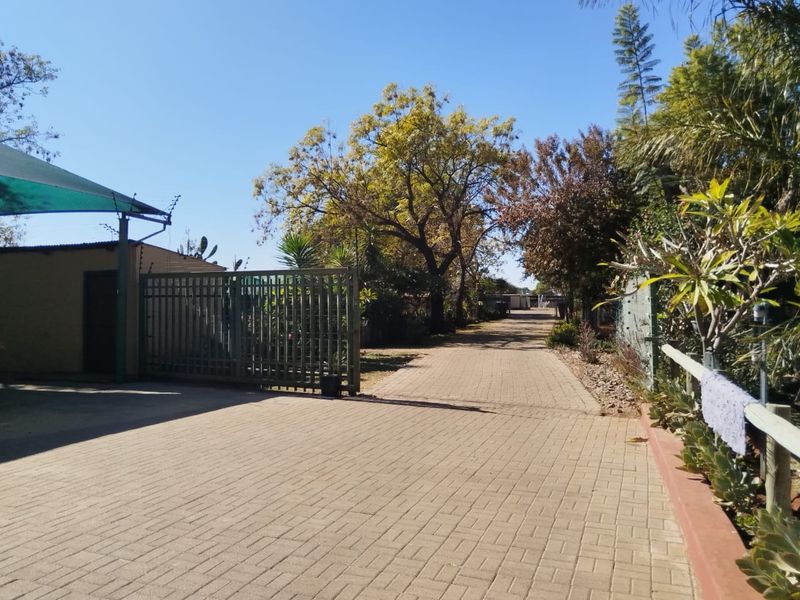 A paved driveway leading to a secure entrance with a metal gate, electric fencing, and a shade cloth carport structure.