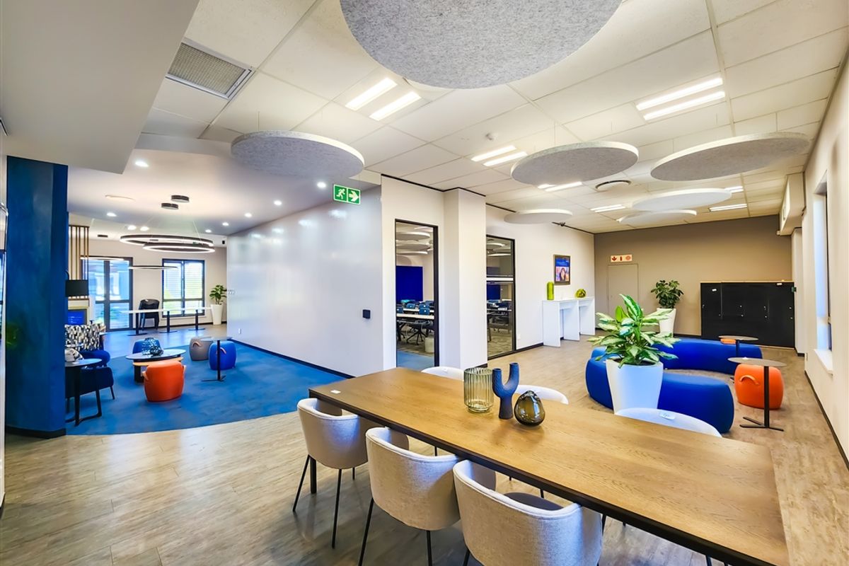 A modern, open-plan office space featuring a mix of wood-look vinyl and carpeted flooring, suspended acoustic ceiling panels, and recessed lighting.