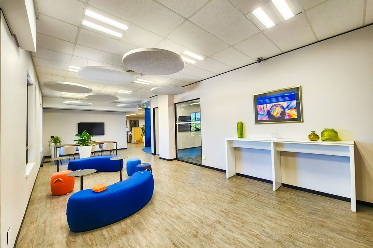Modern open-plan office space featuring suspended acoustic ceiling panels, wood-look flooring, and a glass-partitioned meeting area.