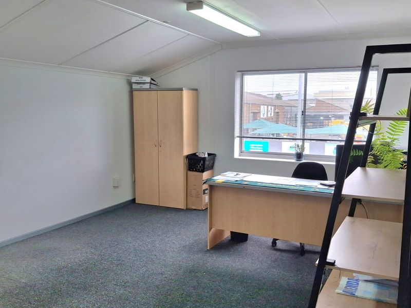 A functional office space featuring carpeted flooring, fluorescent lighting, and a built-in storage cupboard with natural light from the window.