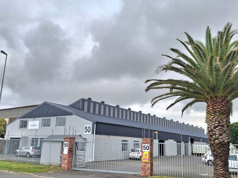 Front elevation of an industrial warehouse property featuring metal cladding, secure perimeter fencing with electric wires, and gated access.