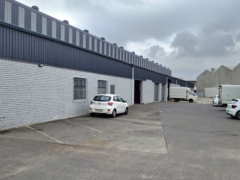 Rear exterior view of an industrial warehouse featuring painted brick walls, metal cladding, and multiple roller shutter access points with an asphalt yard.