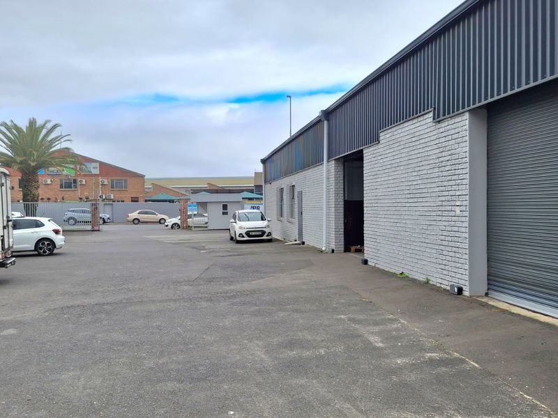 Exterior view of an industrial property featuring a large roller shutter door, painted brick facade, and paved driveway area.