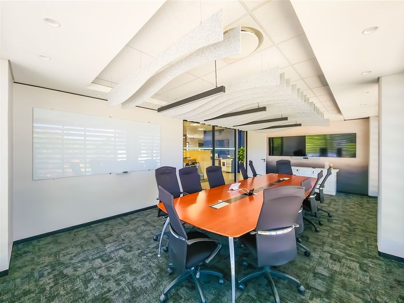 A modern, well-appointed boardroom featuring acoustic ceiling baffles, recessed lighting, a large wall-mounted whiteboard, and glass partitioning for a professional office environment.