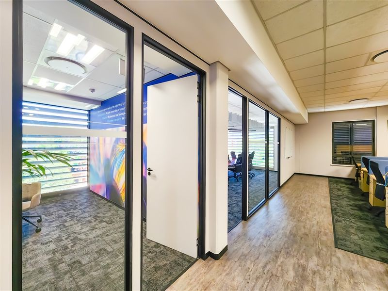 Modern office space featuring glass-partitioned private offices, suspended ceilings, recessed lighting, and a combination of carpet and vinyl flooring.