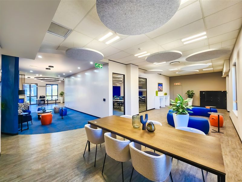 A modern, open-plan office space featuring a mix of wood-look vinyl and carpeted flooring, suspended acoustic ceiling panels, and recessed lighting.