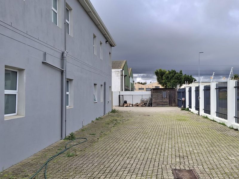 Rear exterior view of the industrial property featuring a paved driveway, perimeter fencing, and external building access.