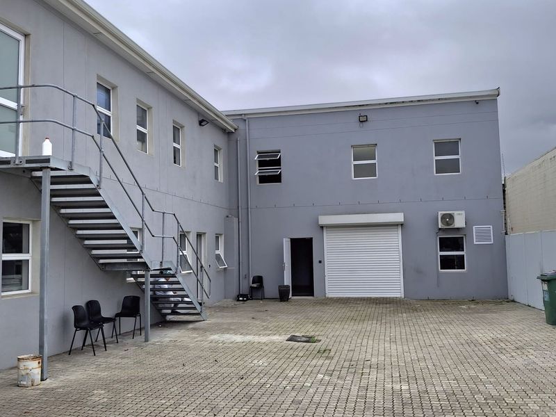 Rear industrial courtyard featuring a paved surface, external metal staircase access, and a roller shutter door for loading access.