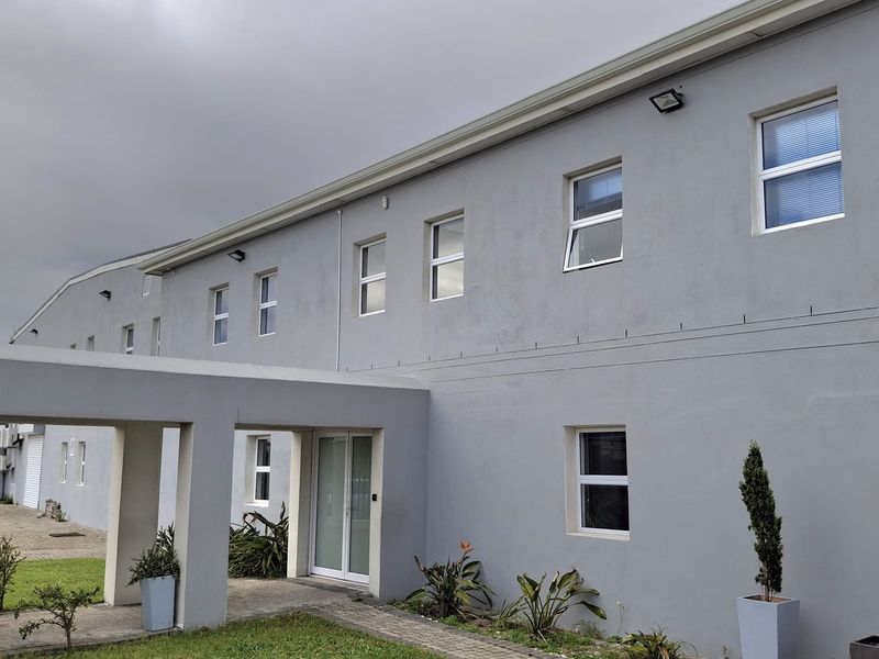 Front elevation of an industrial building featuring a covered entrance walkway, paved access, and multiple casement windows along the grey rendered facade.