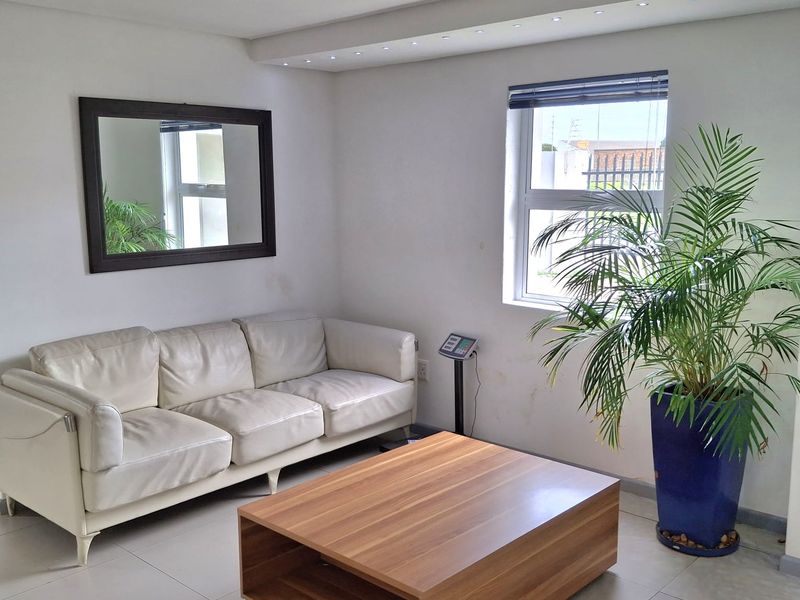 A bright living area featuring tiled flooring, recessed ceiling lighting, and an aluminium window frame, providing a functional space for office or reception use.