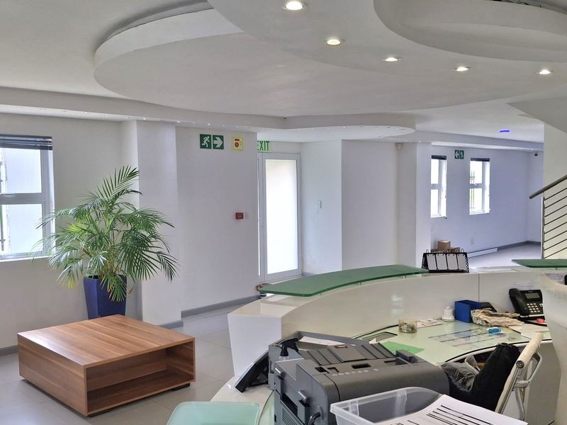 Modern industrial reception area featuring a curved built-in desk, recessed ceiling lighting, and tiled flooring in a bright, professional office space.