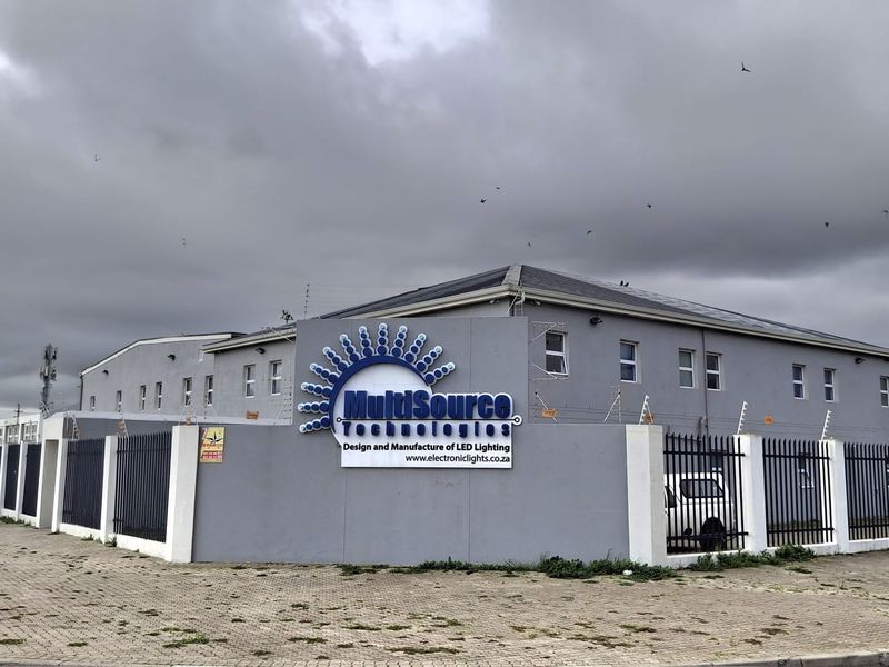 Front exterior view of an industrial property featuring a perimeter wall with electric fencing, secure metal gates, and prominent commercial signage.