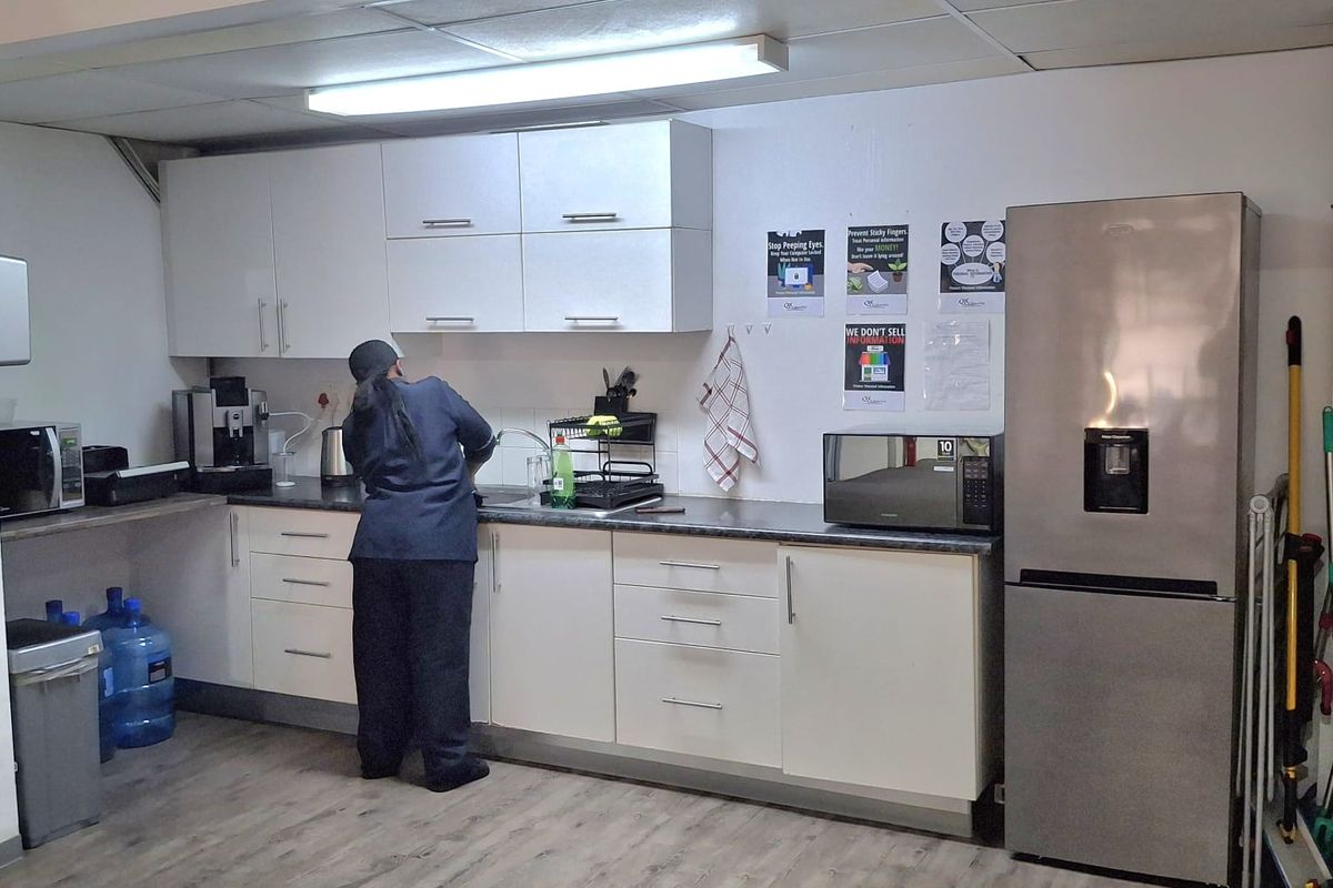 A functional kitchenette area featuring white cabinetry, laminate countertops, and wood-look flooring, suitable for office or industrial staff use.