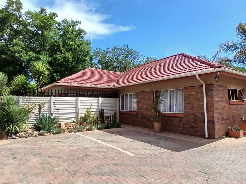 Front exterior view of a brick-faced guest house featuring a tiled roof, paved driveway, and secure boundary walling with established garden landscaping.