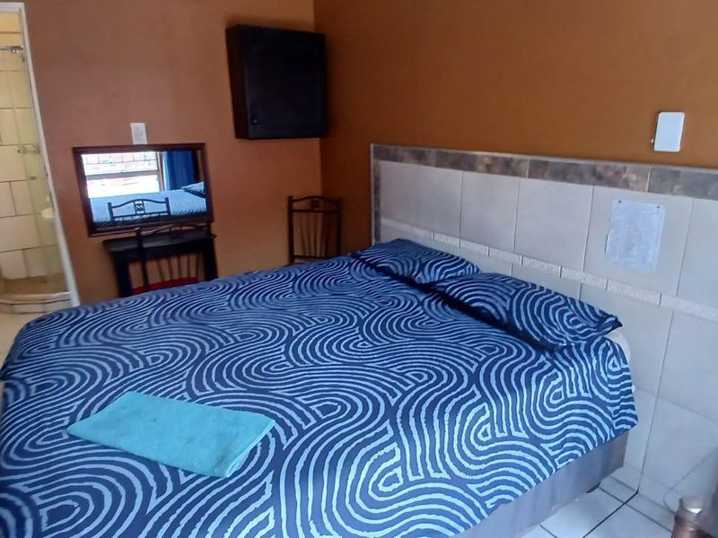 A bedroom featuring a tiled headboard and an attached en-suite bathroom with a glass shower enclosure and ceramic toilet.
