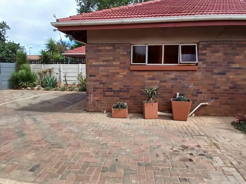 A view of the rear exterior featuring a face brick facade, tiled roof, and paved driveway area with a secure boundary wall.