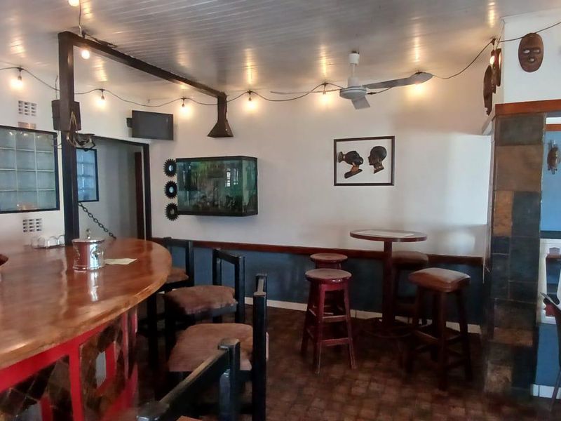 A rustic bar area featuring a curved wooden counter, tiled flooring, and a beadboard ceiling, providing a cozy space for entertainment.