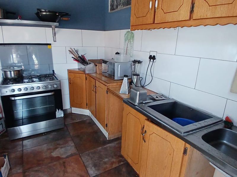 A functional kitchen featuring wooden cabinetry, a gas stove with oven, double stainless steel sink, and tiled backsplash.