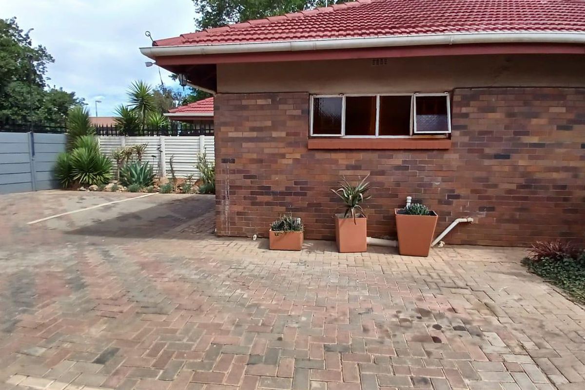 A view of the rear exterior featuring a face brick facade, tiled roof, and paved driveway area with a secure boundary wall.