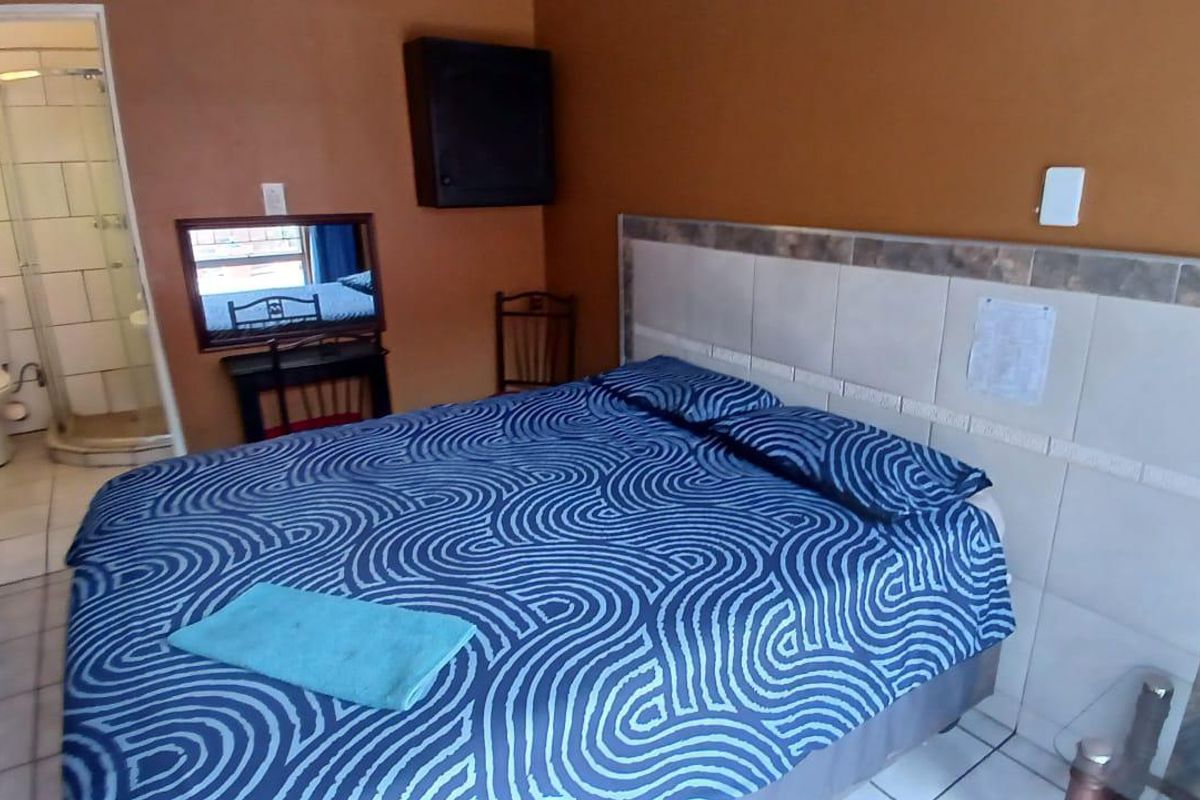 A bedroom featuring a tiled headboard and an attached en-suite bathroom with a glass shower enclosure and ceramic toilet.