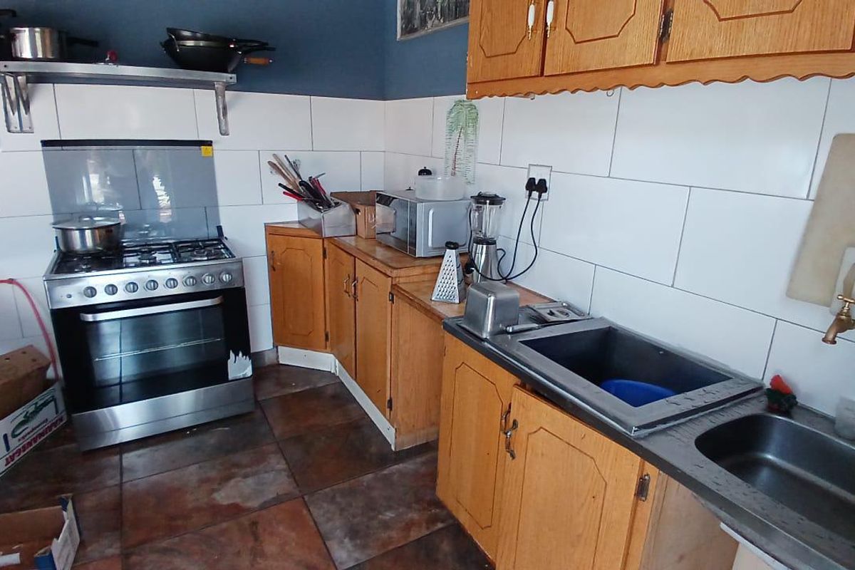 A functional kitchen featuring wooden cabinetry, a gas stove with oven, double stainless steel sink, and tiled backsplash.