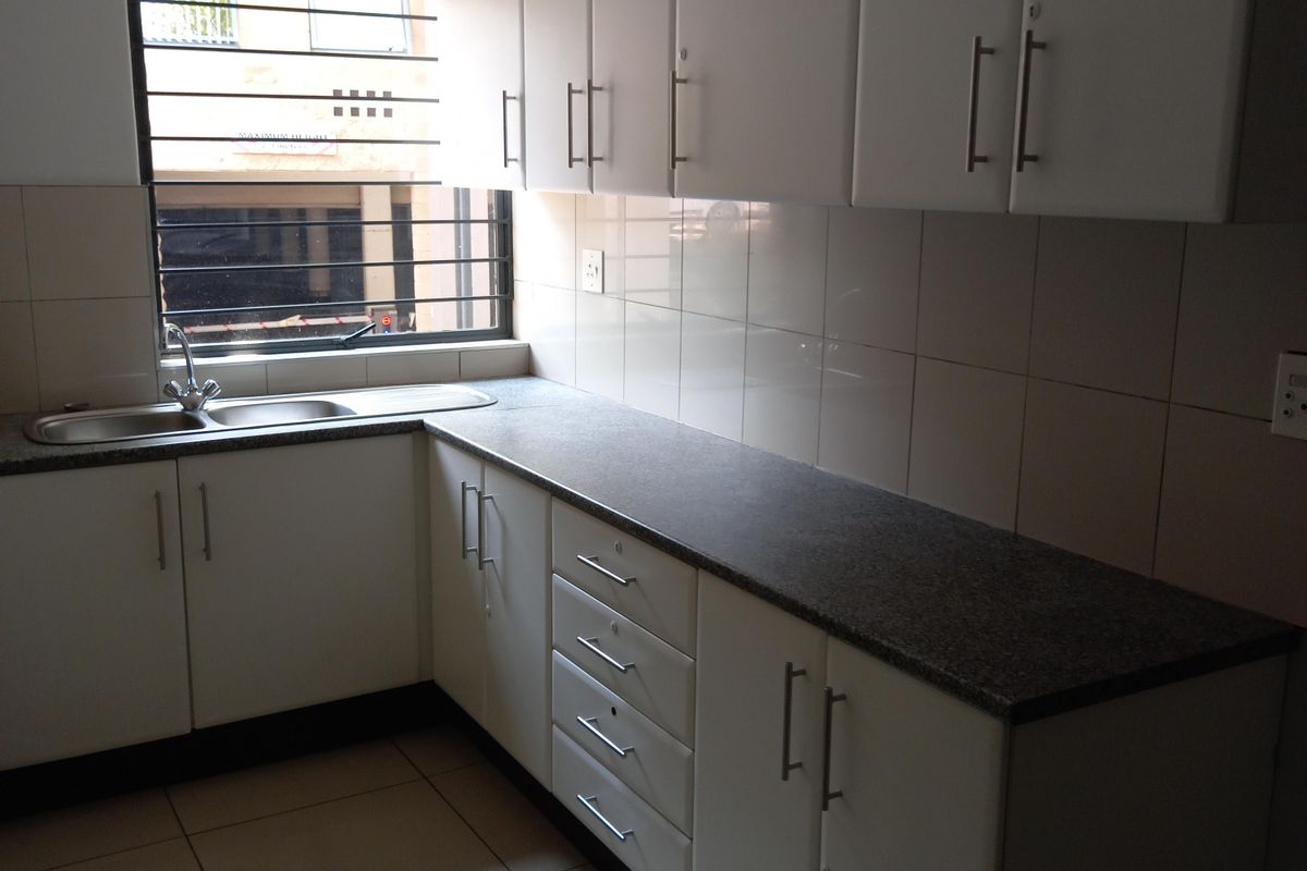 A functional office kitchenette featuring white cabinetry, granite countertops, a stainless steel sink, and tiled flooring.