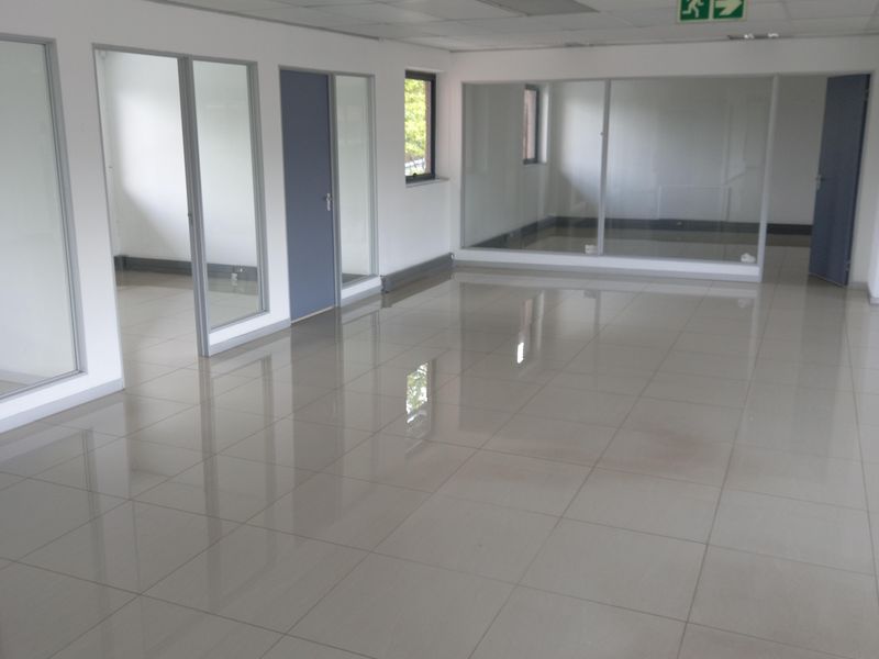 A bright, open-plan office space featuring polished tile flooring, glass partitions, and a suspended ceiling with integrated lighting.