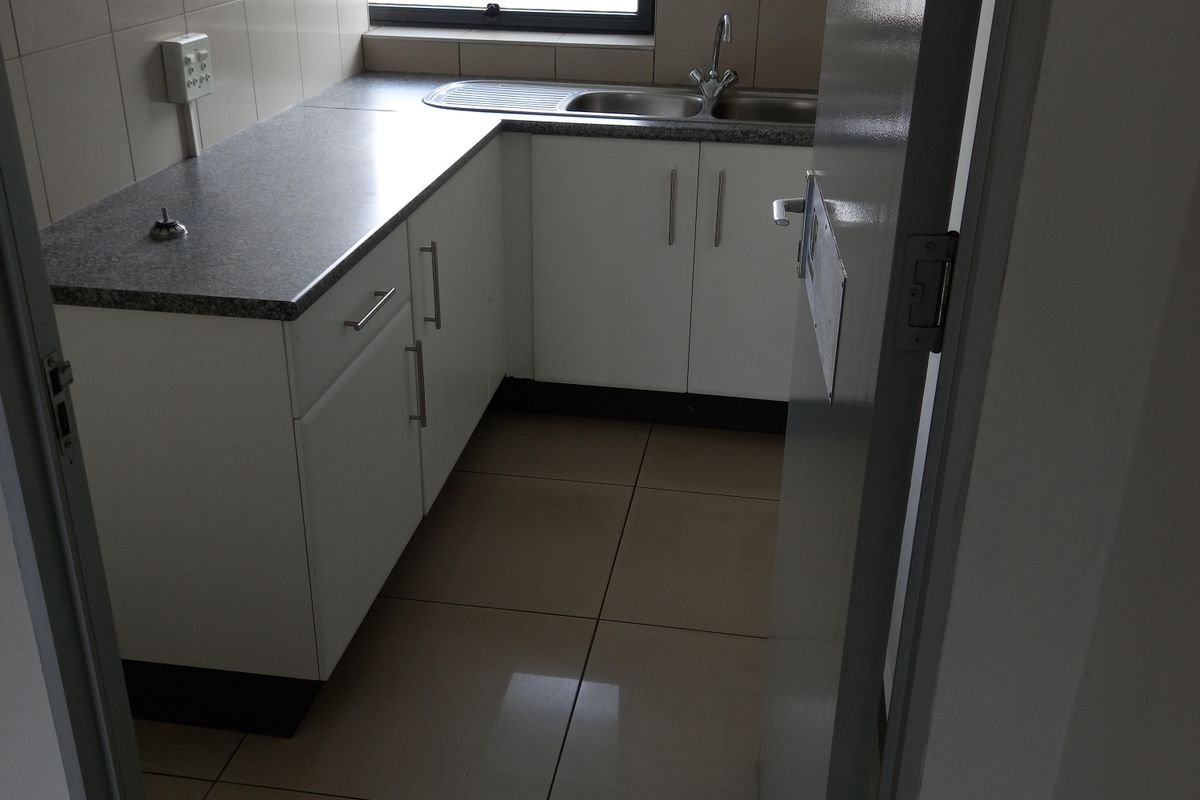 A compact, functional office kitchenette featuring white built-in cabinetry, laminate countertops, a stainless steel sink, and tiled flooring.