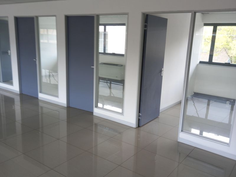A bright, modern office space featuring polished tiled flooring, suspended ceilings, and multiple glass-partitioned private offices.