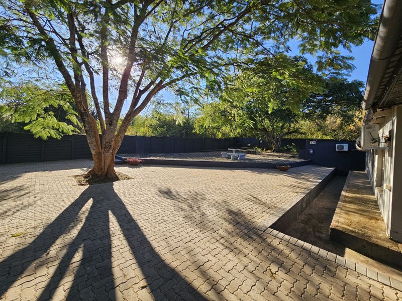 Spacious paved rear courtyard area featuring mature trees, perimeter fencing, and a retaining wall, providing a functional outdoor space for the guest house.