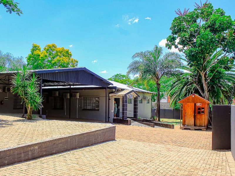 Front exterior view of the guest house featuring a paved driveway, covered patio area, and established garden surroundings.