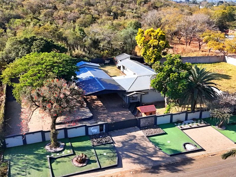 Aerial view of the guest house property featuring a paved driveway, perimeter wall, covered carport, and landscaped grounds with artificial turf.
