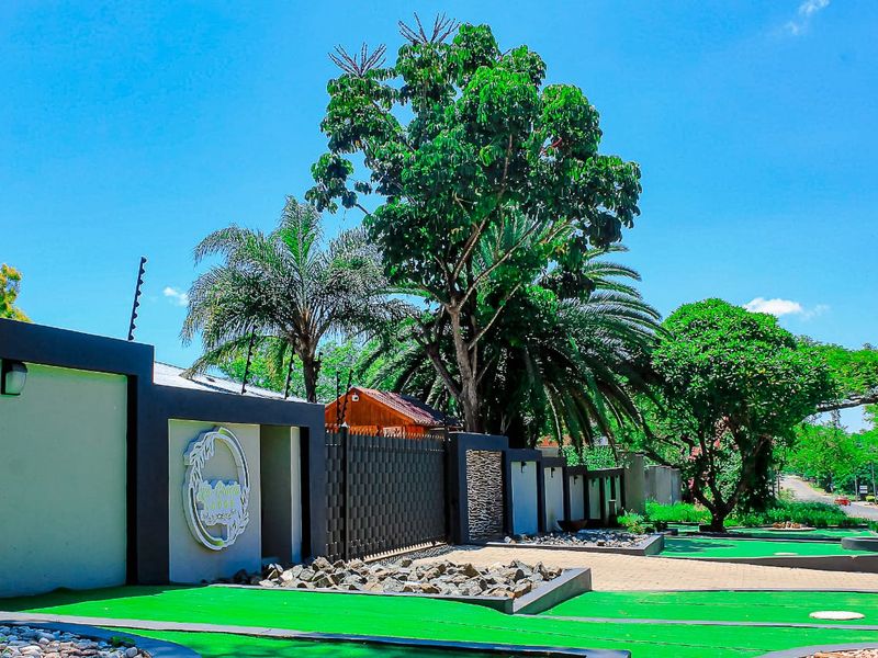 Front exterior view of the guest house property featuring a paved entrance, boundary wall with electric fencing, and well-maintained garden landscaping.