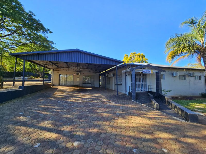 Front exterior view of the guest house featuring a large paved driveway, covered carport, and a designated reception entrance with ramp access.