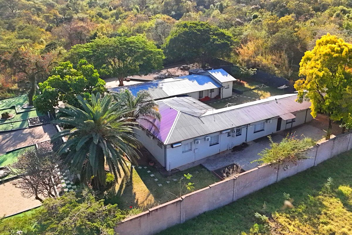 Aerial view of the guest house property featuring a metal roof, perimeter wall, and established garden surroundings.