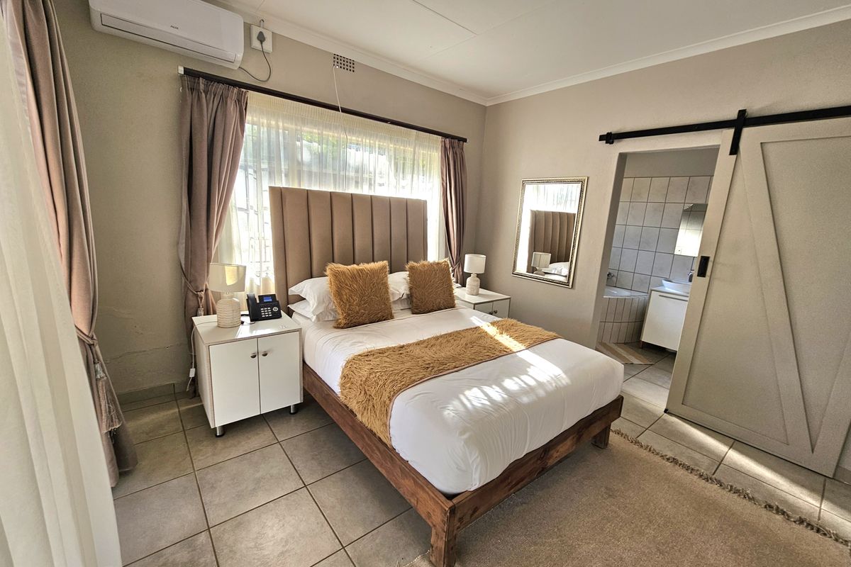 A well-maintained bedroom featuring tiled flooring, a split-system air conditioner, and a sliding barn door providing access to an en-suite bathroom.