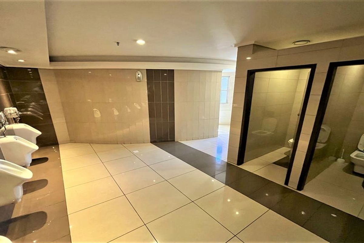 A modern commercial office restroom featuring tiled flooring, wall-mounted urinals, and private toilet cubicles with glass doors.