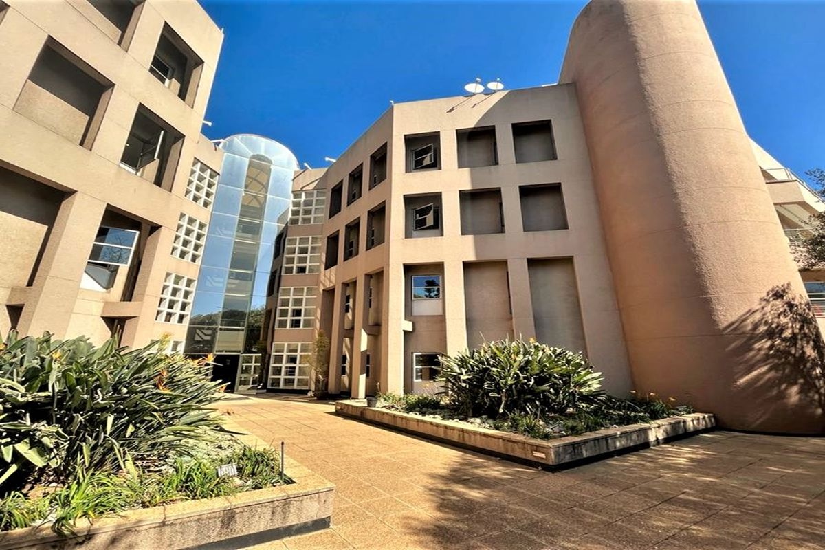 Exterior view of a modern multi-story office building featuring a glass atrium, concrete facade, and landscaped courtyard area.
