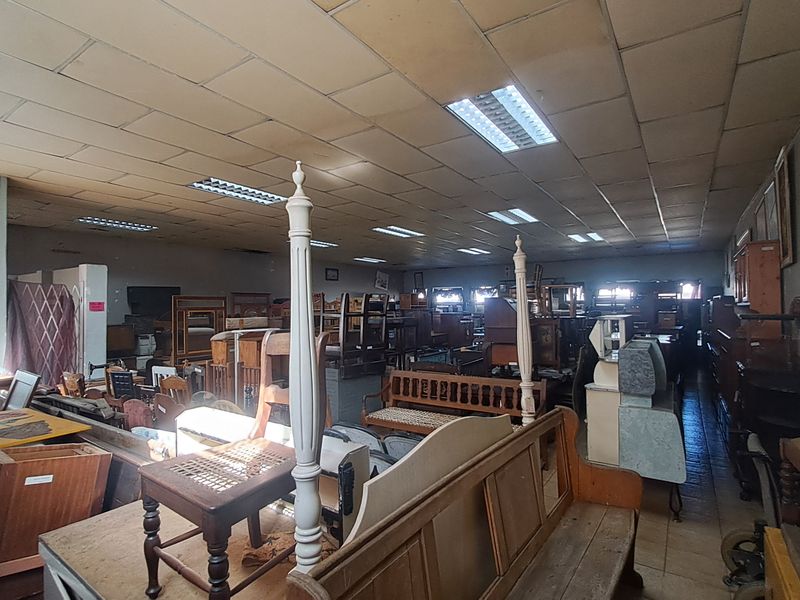 A large retail space featuring a suspended ceiling with recessed fluorescent lighting and tiled flooring, currently utilized for furniture storage.