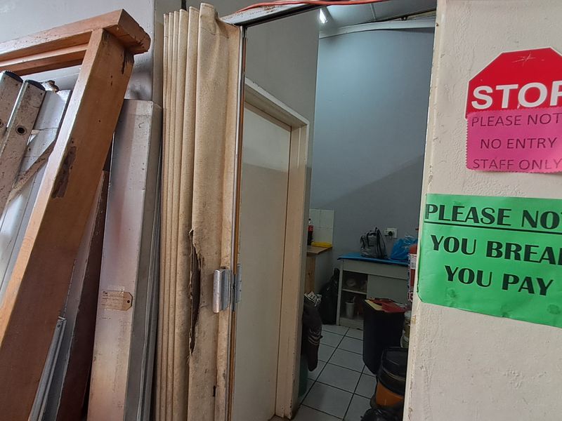 A utility or storage area accessed via a damaged folding door, featuring tiled flooring and basic built-in cabinetry.