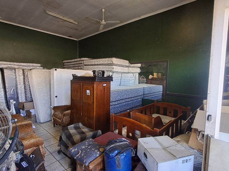 A cluttered retail or storage space featuring tiled flooring, ceiling fans, and fluorescent lighting, currently used for inventory storage.