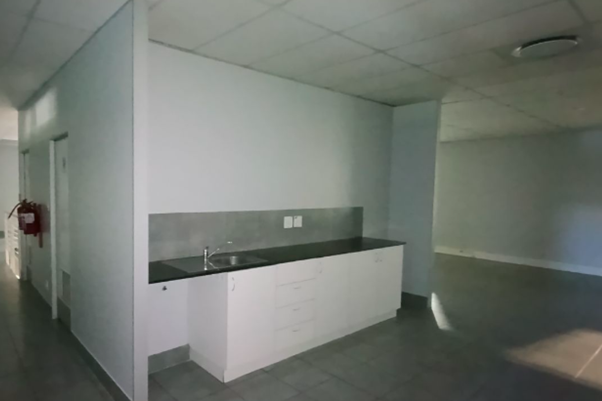 A functional kitchenette area featuring built-in white cabinetry, a stainless steel sink, and tiled flooring within an open-plan industrial office space.
