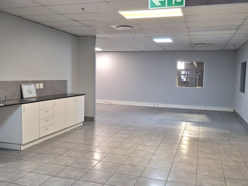 A clean, open-plan industrial utility space featuring tiled flooring, a functional kitchenette area, and suspended ceiling with integrated lighting.