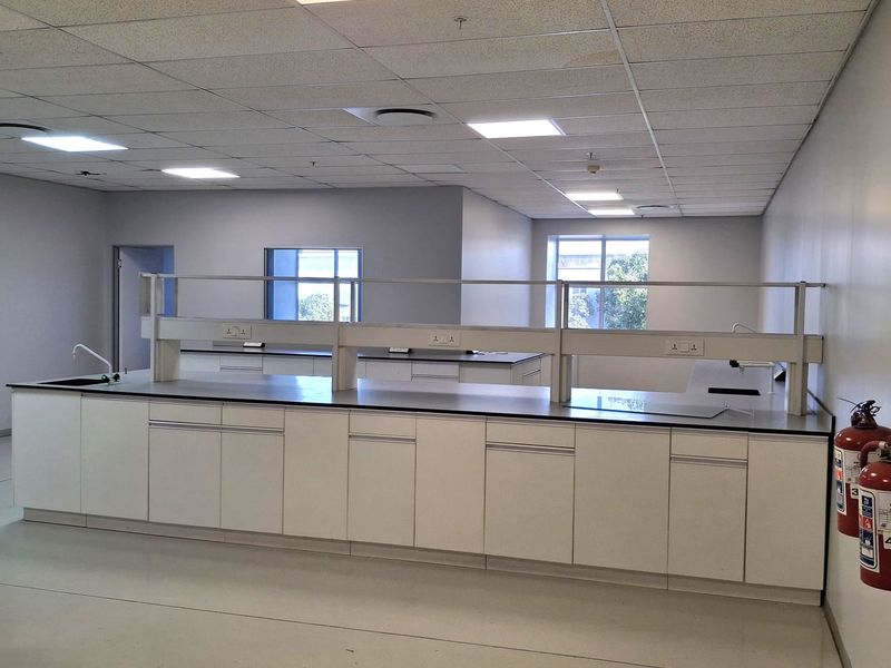 A clean, modern industrial laboratory space featuring built-in cabinetry, integrated worktops, sink, and professional suspended ceiling lighting.