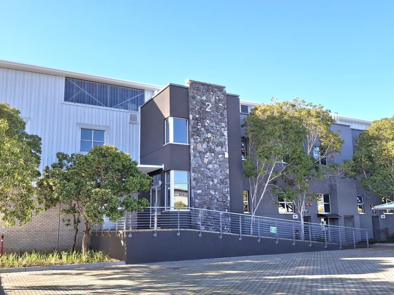 Modern industrial building facade featuring a stone-clad entrance, metal cladding, and a paved parking area with an accessible ramp.