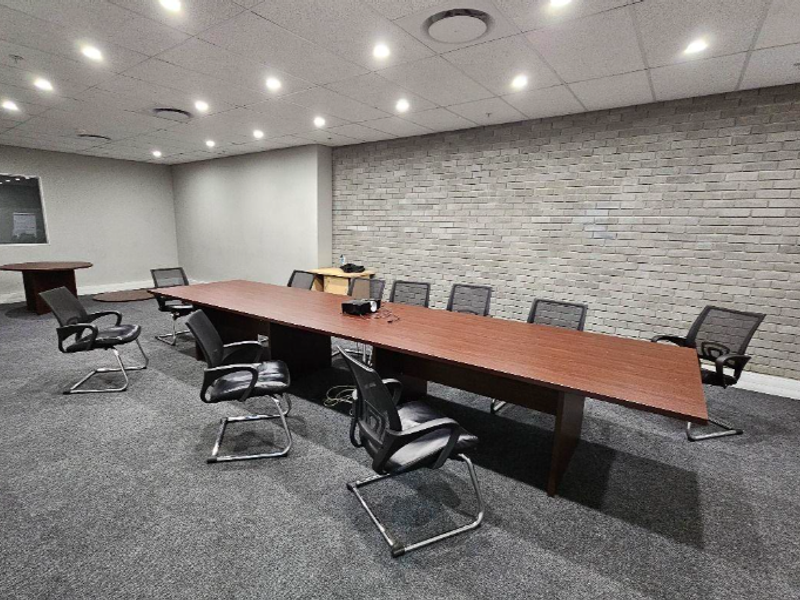 A professional office boardroom featuring a suspended ceiling with recessed lighting, a textured brick feature wall, and carpeted flooring.
