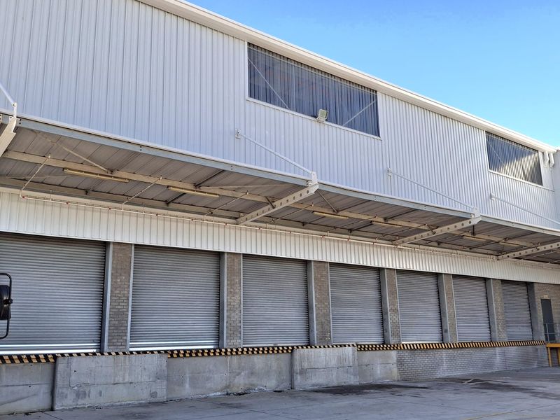 Industrial warehouse exterior featuring multiple roller shutter loading doors, a protective canopy, and a durable concrete loading apron.