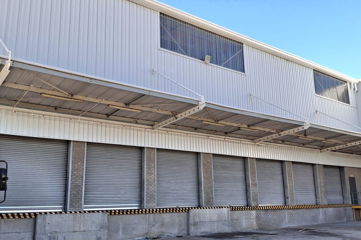 Industrial warehouse exterior featuring multiple roller shutter loading doors, a protective canopy, and a durable concrete loading apron.