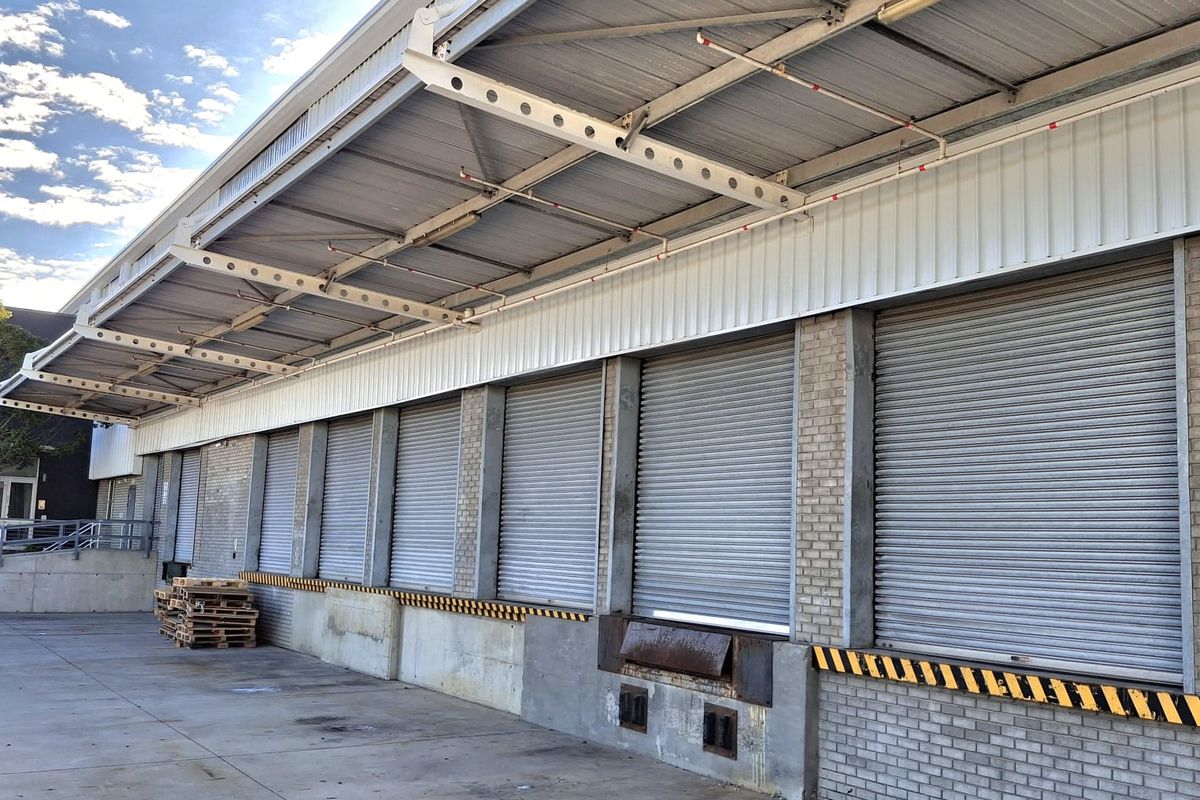 Industrial loading bay area featuring multiple roller shutter doors, a protective metal canopy, and a concrete loading apron.